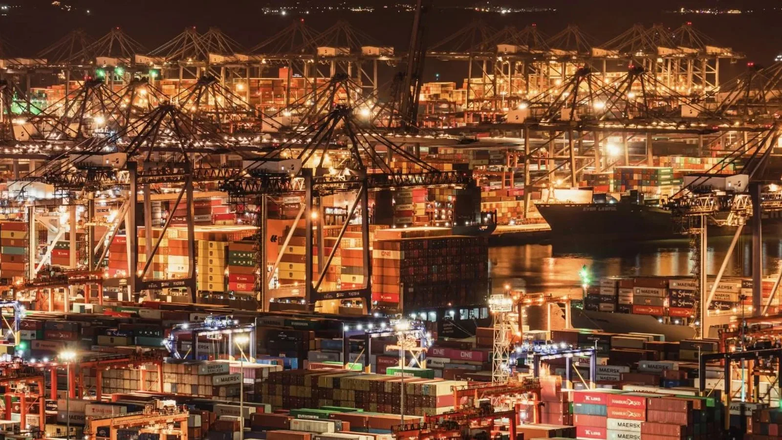 Terminal portuaria iluminada operando de noche con grúas y contenedores